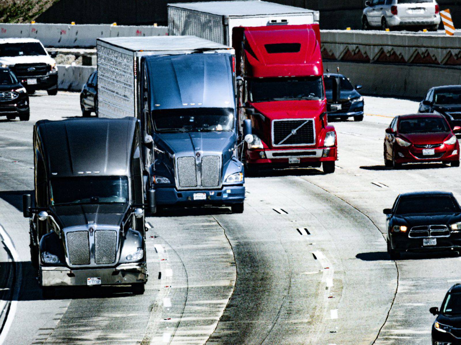 Tractor-trailers and passenger vehicles travelling together on a multi-lane highway.