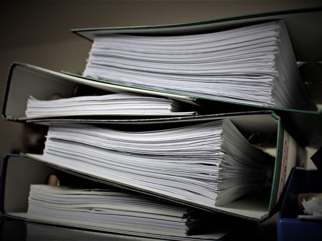 A stack of ring binders filled with paperwork, representing maintained program records.